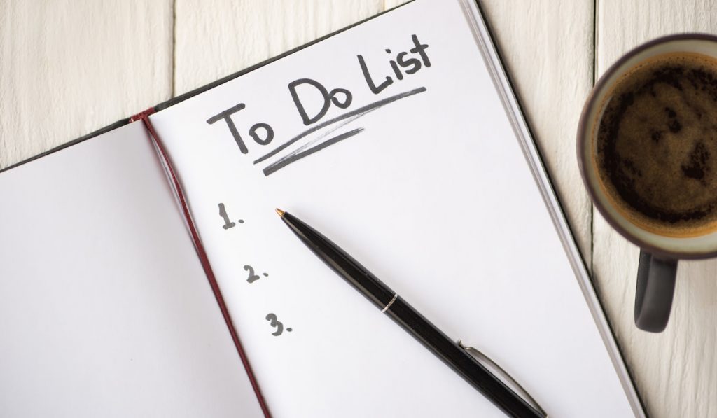 Top view of notebook with do list lettering and pen near cup of coffee on wooden background