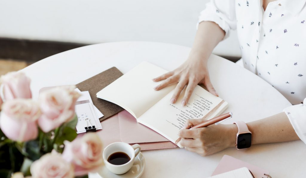 Young woman writing a journal with coffee, smart watch, white table