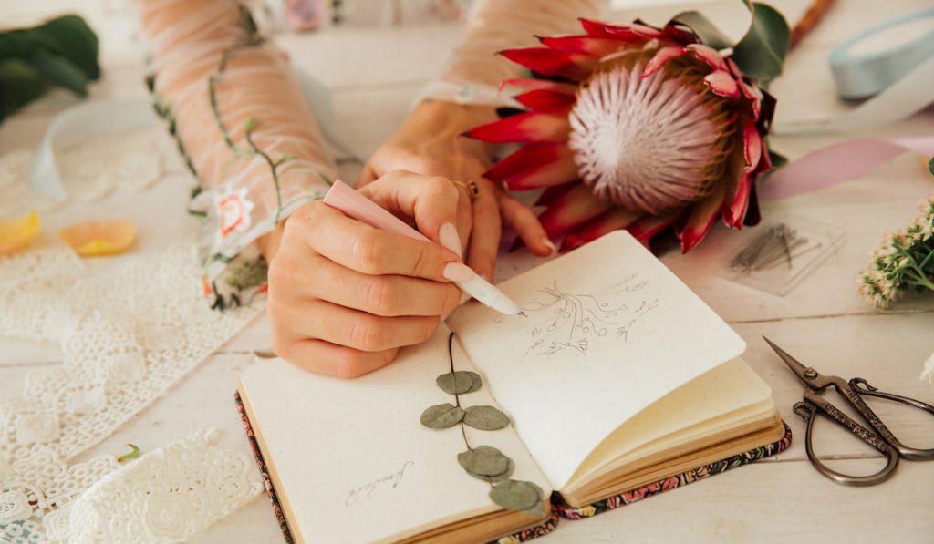woman drawing on her journal with scissor and flower on the table