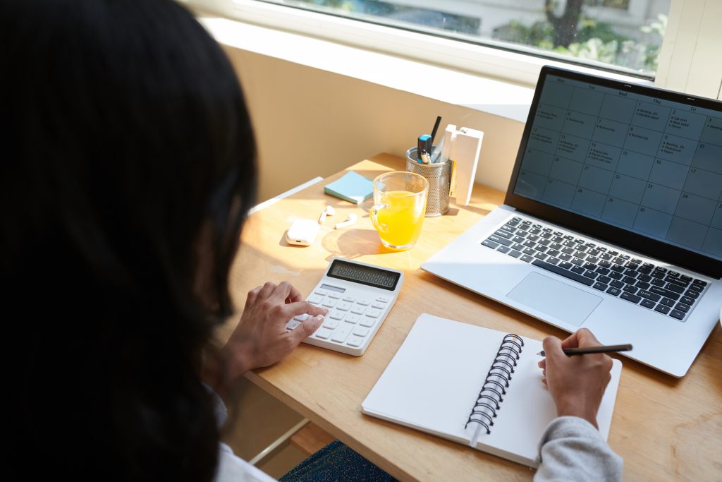 Female entrepreneur checking planner on laptop and making calculation when working from home due to pandemic