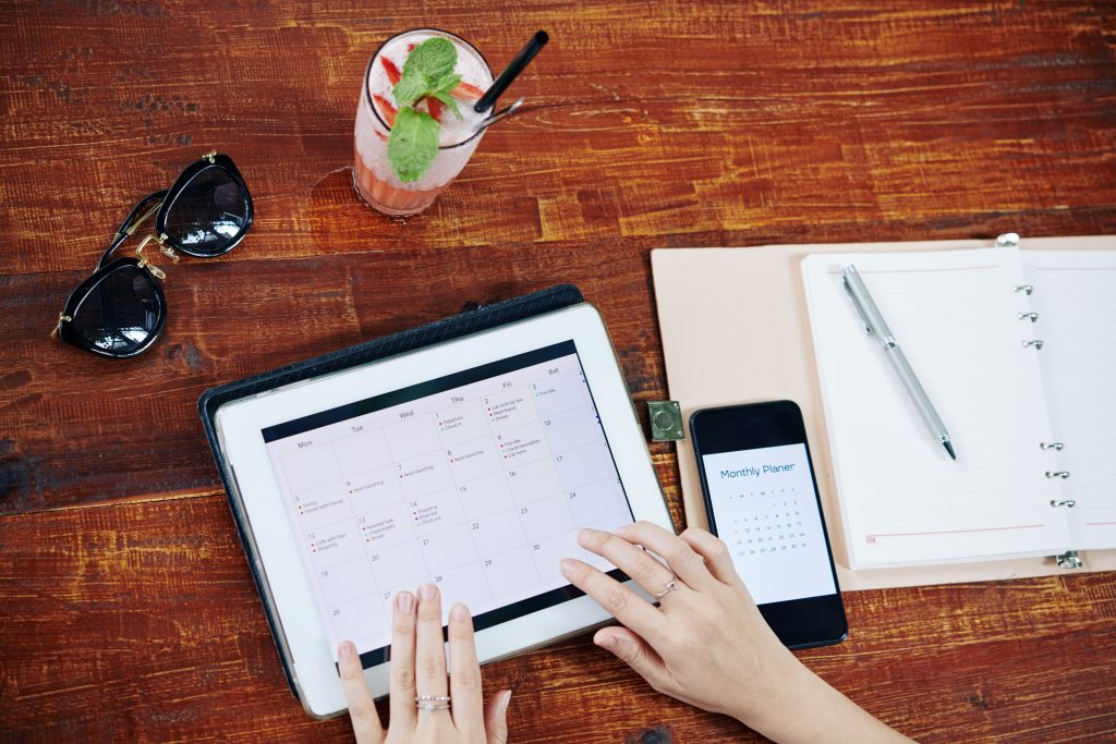 Woman checking planner app with drink and shades on the table