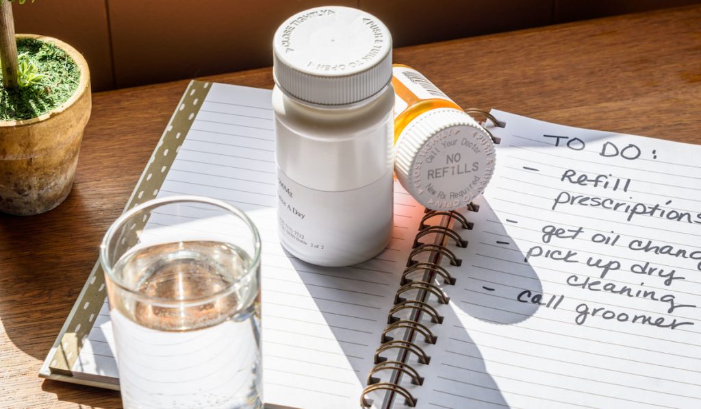 daily to do list on a planner and pill bottles with water glass on the table