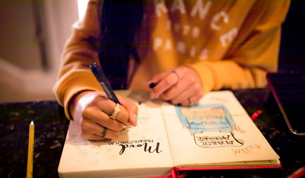 Closeup of young teen girl writing in bullet journal on mood tracker page

